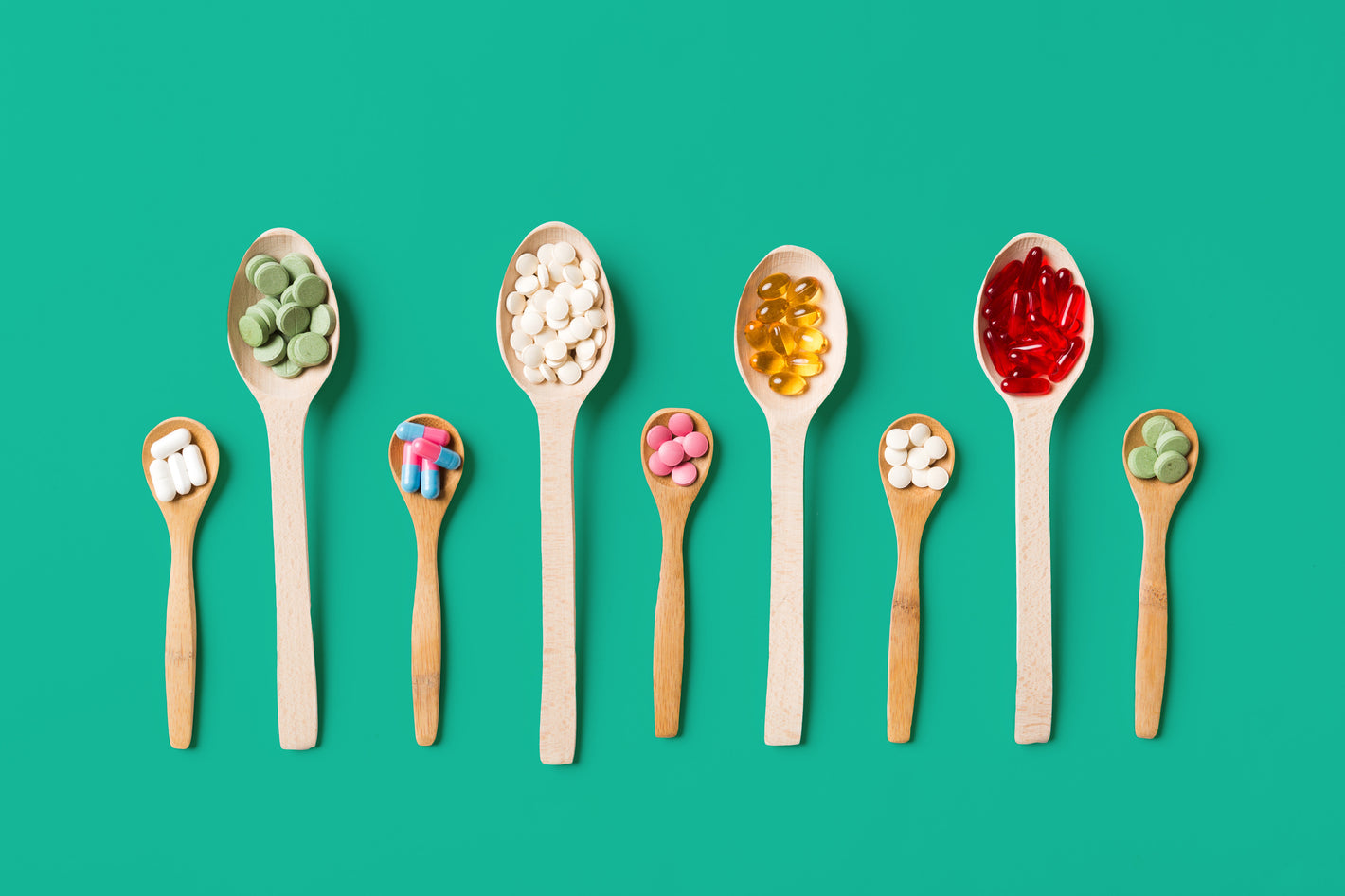 Various vitamin and supplement pills, tablets and capsules arranged on wooden spoons